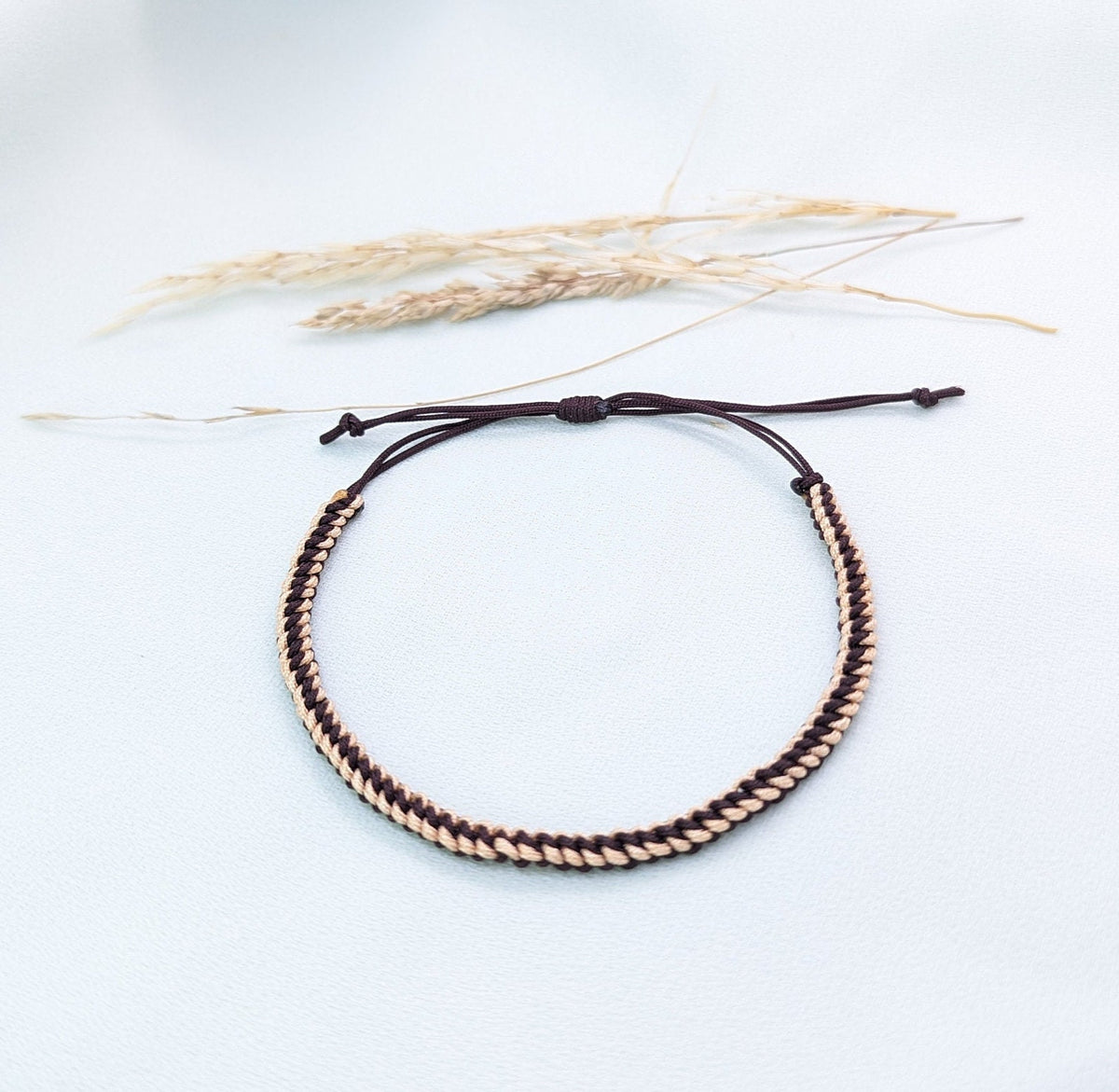 Brown and caramel woven surfer bracelet with adjustable brown cord, on a white background