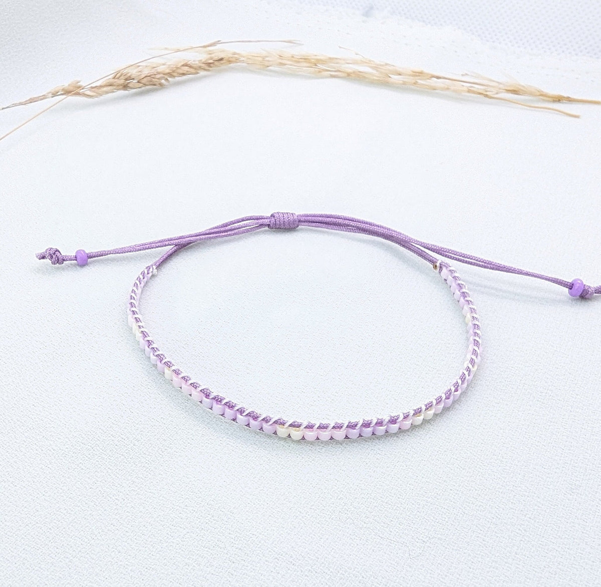 Lilac and white beaded macramé bracelet with lilac adjustable cords, on a pale background