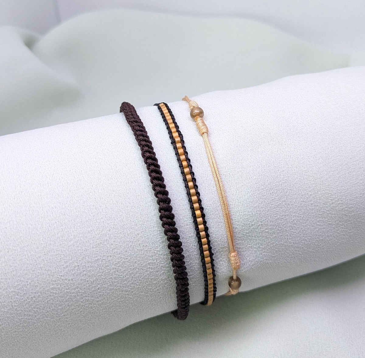 Set of three bracelets in brown, black and caramel with small gold beads, shown on a white roll