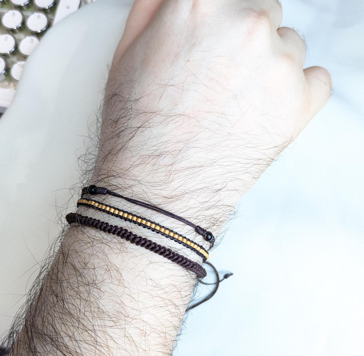 Stack of three thin black and gold beaded cord bracelets worn on a man's wrist