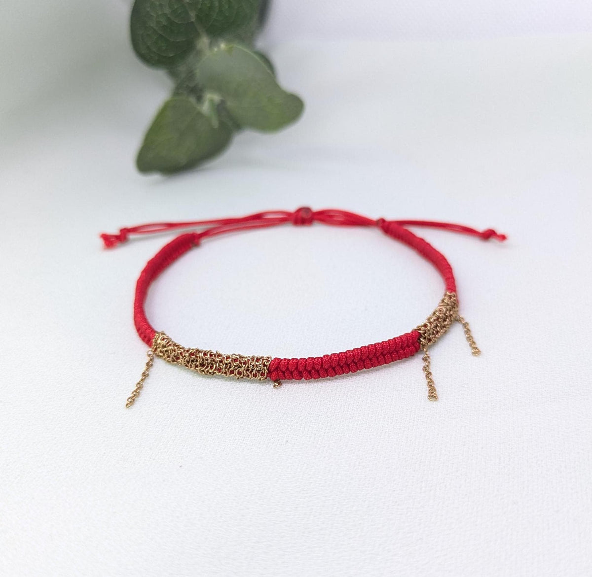 Red woven bracelet with gold chain sections and small chain tassels, sliding knot closure