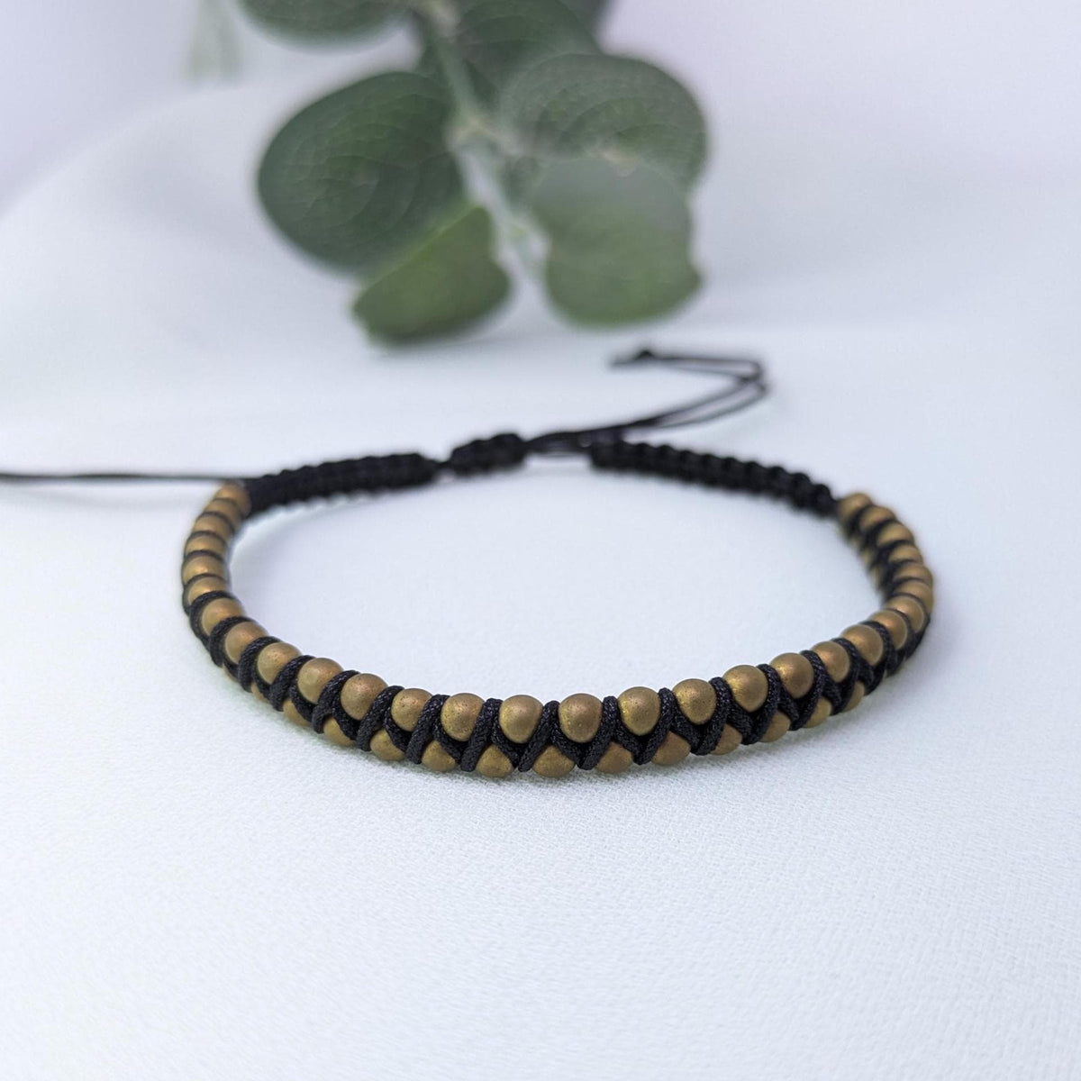 Bronze and black beaded bracelet woven on black cord with an adjustable sliding knot, on a white surface